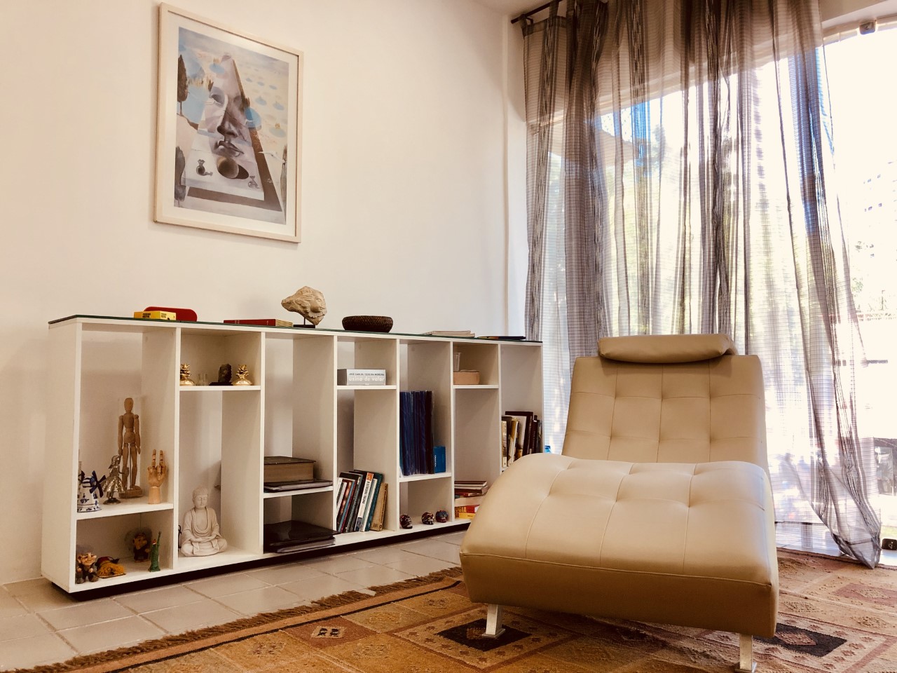 Sala de atendimento do consultório, com chaise e estante de livros